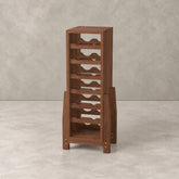 A tall wooden wine rack with multiple staggered bottle-holding shelves and a lower open storage compartment, shown in a warm medium-brown finish against a textured light gray studio backdrop.