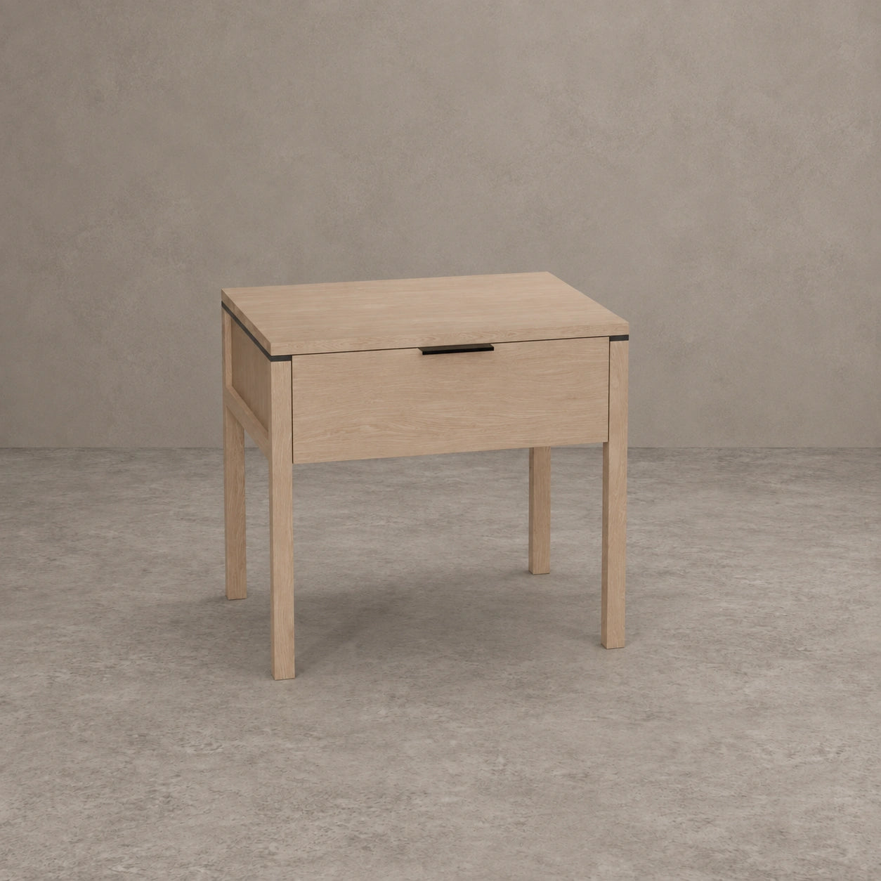 A light oak wood nightstand with a single drawer, featuring a minimalist black metal pull handle and slim black metal corner accents, set against a textured gray concrete wall and floor.