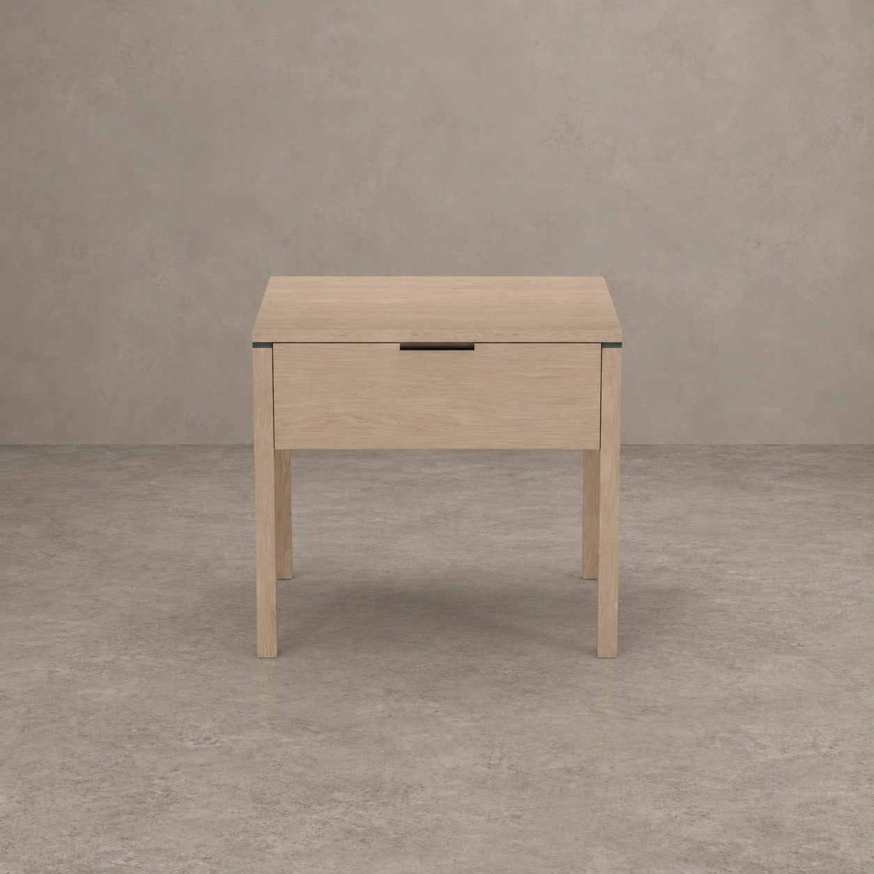 A light natural wood nightstand with a single drawer and a slim black metal pull handle, set against a textured gray concrete wall and floor.