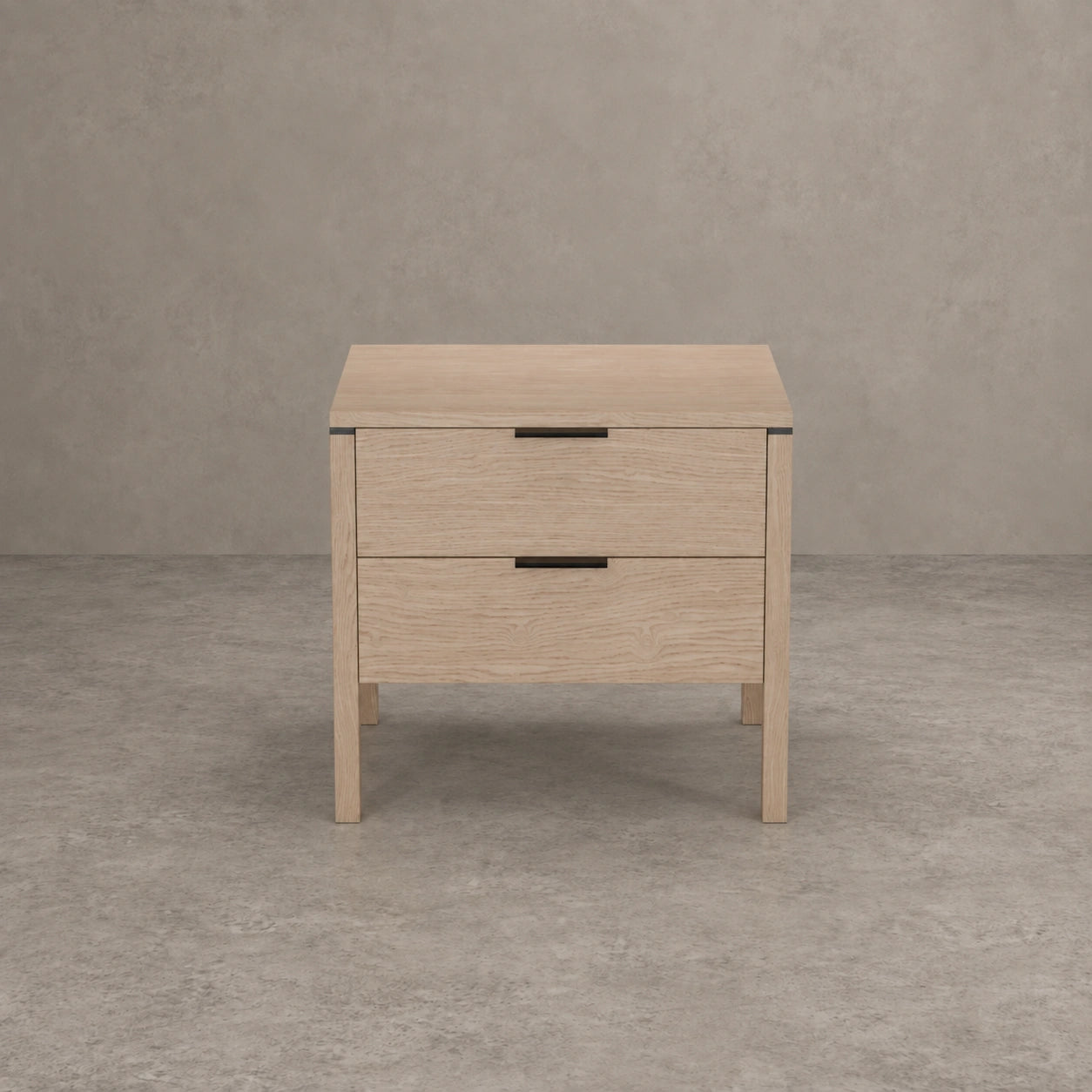 A light oak wood two-drawer nightstand with black metal handles, shown from a front-facing perspective against a textured gray concrete wall and floor.