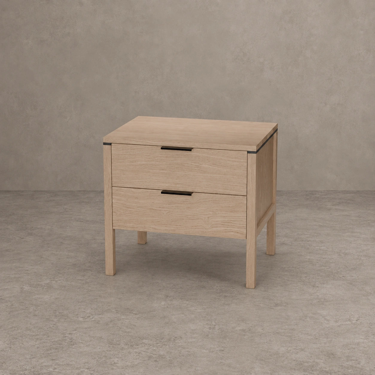 A light oak wood two-drawer nightstand with black metal drawer pulls, shown on a textured gray concrete floor against a matching gray wall.