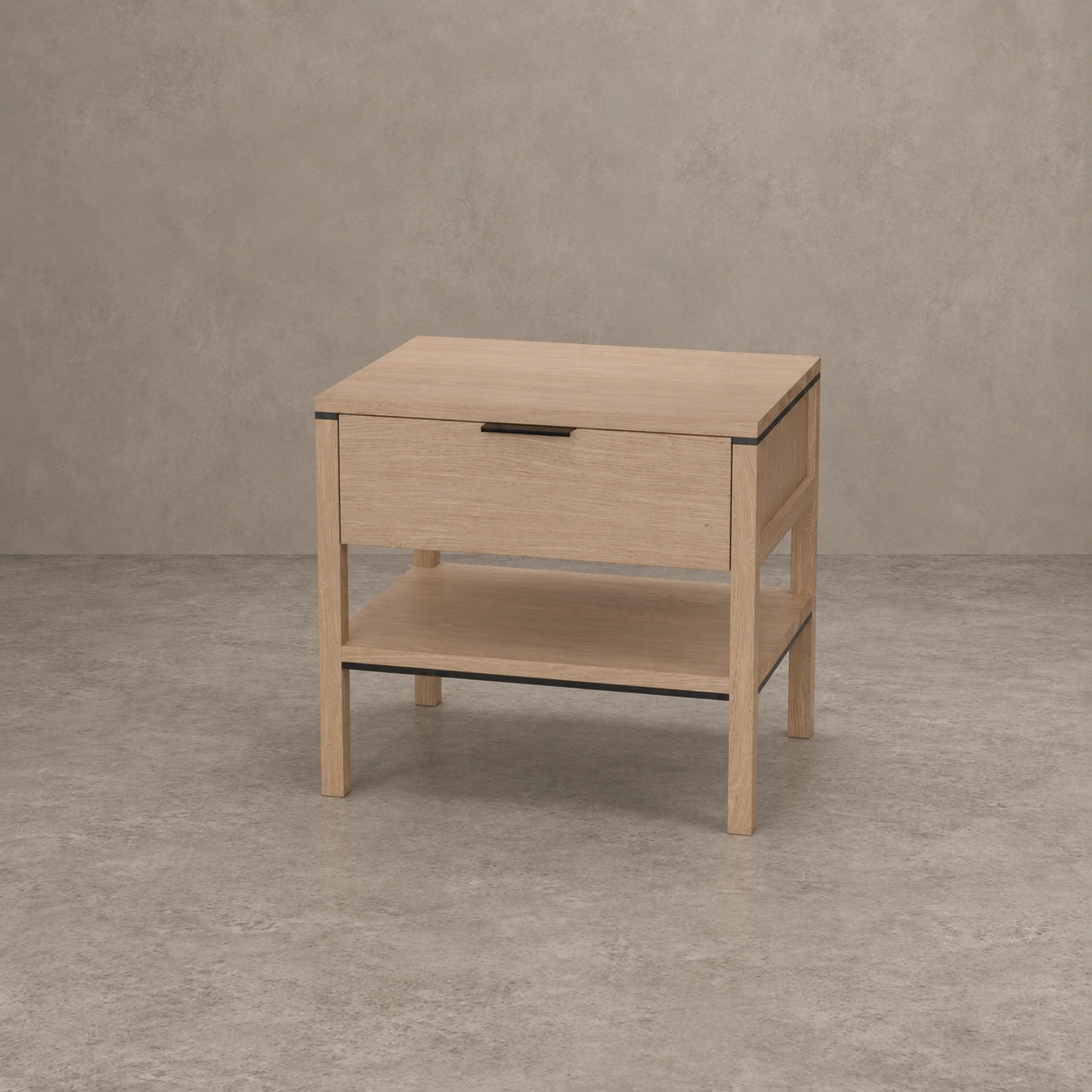 A light oak wood nightstand with a single drawer, open lower shelf, and slim black metal handle, set against a textured gray concrete wall and floor.